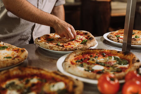 Pizzaiolo garneert versgebakken pizza’s met basilicum in de keuken.
